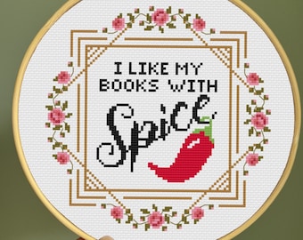 May include: A white embroidery hoop with a red chili pepper and the text "I like my books with spice" in black lettering. The hoop is decorated with a floral border of pink roses.