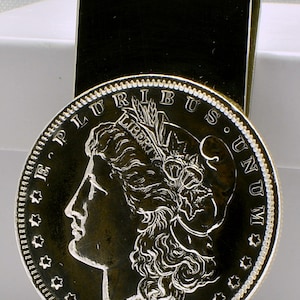May include: Silver dollar money clip featuring a profile of Lady Liberty with the inscription "E PLURIBUS UNUM" and the year "1880".