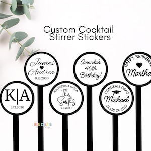 May include: Six black and white round cocktail stirrer stickers with various personalized text, including names, dates, and messages. The stickers are attached to black sticks.