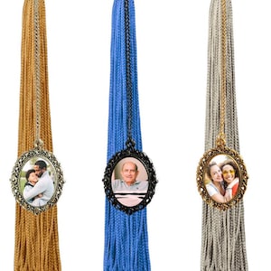 May include: Three graduation tassel charms with oval-shaped photo frames. The frames are gold, black, and silver. Each frame has a different photo of a person or people.