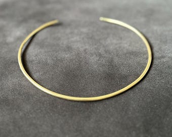 May include: A simple gold choker necklace, a thin band of metal that sits close to the neck.