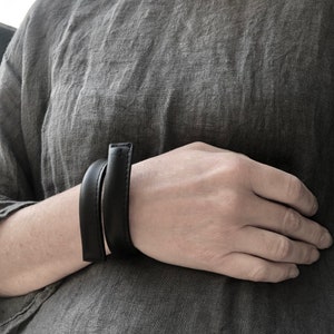 Peut inclure: Un bracelet en cuir noir simple porté au poignet.