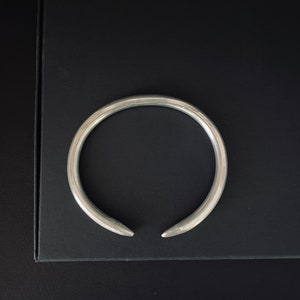 Może przedstawiać: Srebrna bransoletka metalowa o zaokrąglonym, otwartym wzorze.