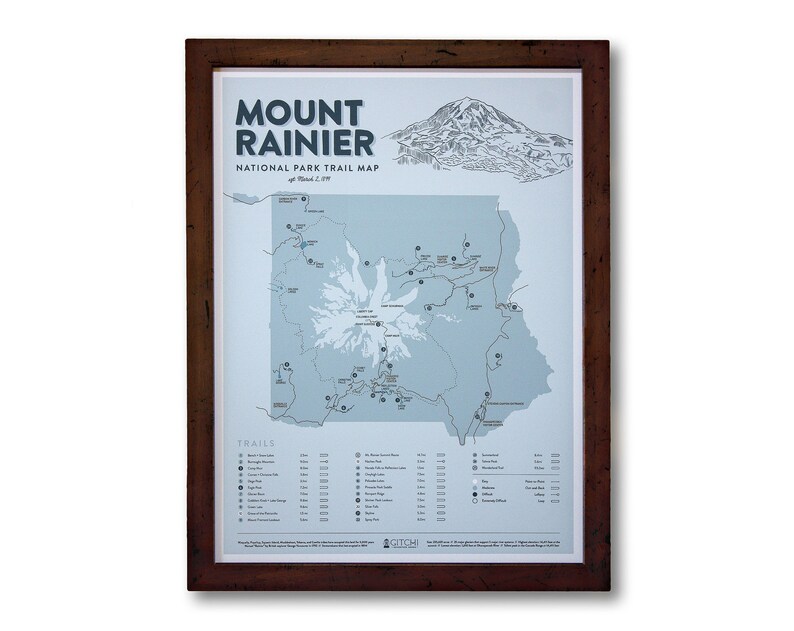 May include: A framed map of Mount Rainier National Park in Washington State. The map shows the location of trails, campgrounds, and other points of interest. The map is printed on a light blue background with dark blue lines and text. The frame is brown wood.