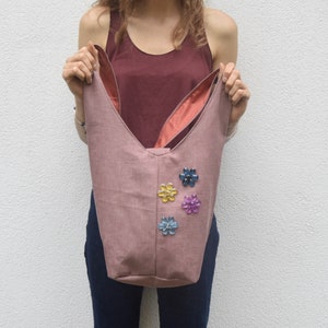 May include: A pink fabric tote bag with a unique bunny ear design. The bag has a pink lining and is decorated with colorful flower embellishments.