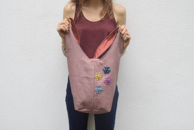 May include: A pink fabric tote bag with a unique bunny ear design. The bag has a pink lining and is decorated with colorful flower embellishments.