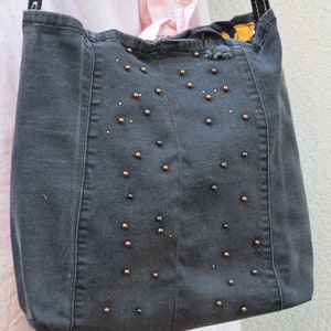 May include: A gray denim tote bag with black and copper colored beads sewn onto the front.