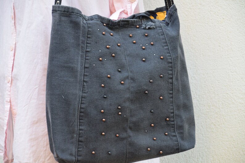 May include: A gray denim tote bag with black and copper colored beads sewn onto the front.