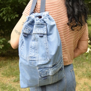 May include: A blue denim drawstring backpack with multiple pockets and a blue strap.