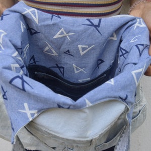 May include: A blue denim bag with a white and blue patterned lining. The bag is open and the lining is visible. The bag has a zippered pocket on the inside.