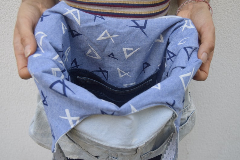 May include: A blue denim bag with a white and blue patterned lining. The bag is open and the lining is visible. The bag has a zippered pocket on the inside.