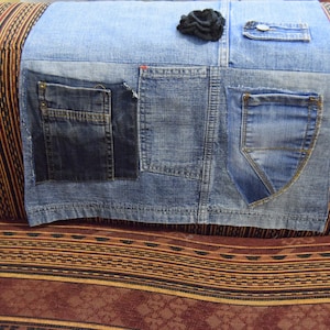 May include: A denim cushion cover with multiple pockets and a black flower embellishment. The cushion cover is placed on a striped couch.