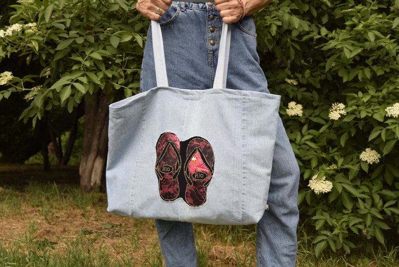 May include: A light blue denim tote bag with two red and black flip-flop patches that say "Rio" on them.