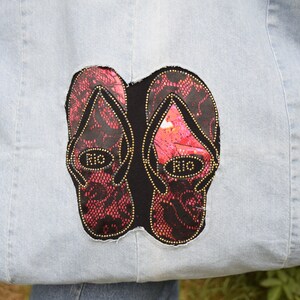 May include: A light blue denim tote bag with a black and red embroidered design of two flip flops. The flip flops have gold accents and the word "Rio" written on them.