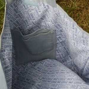 May include: A light blue tote bag with a white and blue patterned lining. The bag has a large pocket on the inside.