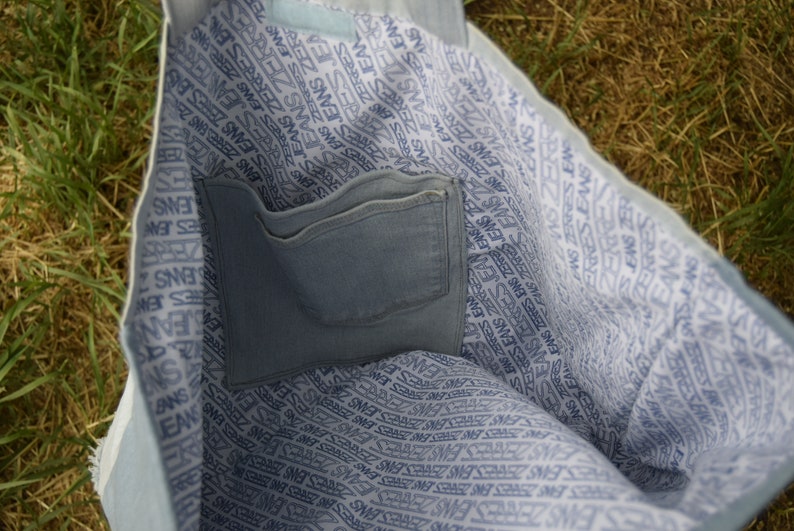 May include: A light blue tote bag with a white and blue patterned lining. The bag has a large pocket on the inside.