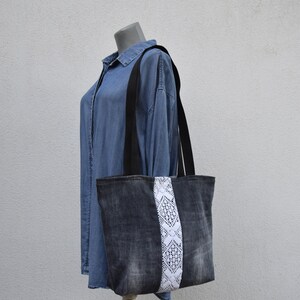 May include: A black denim tote bag with a white lace trim. The bag has black straps and is made of a recycled material.