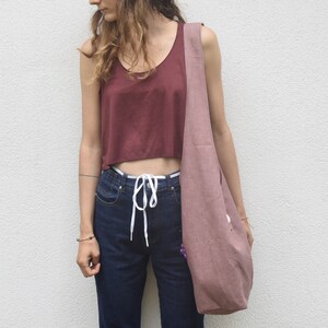 May include: A woman wearing a maroon tank top and blue jeans with a white drawstring. She is carrying a large, dusty pink tote bag.