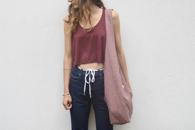 May include: A woman wearing a maroon tank top and blue jeans with a white drawstring. She is carrying a large, dusty pink tote bag.