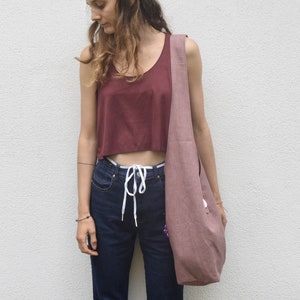 May include: A woman wearing a maroon crop top, blue jeans, and a light pink tote bag with a white drawstring.