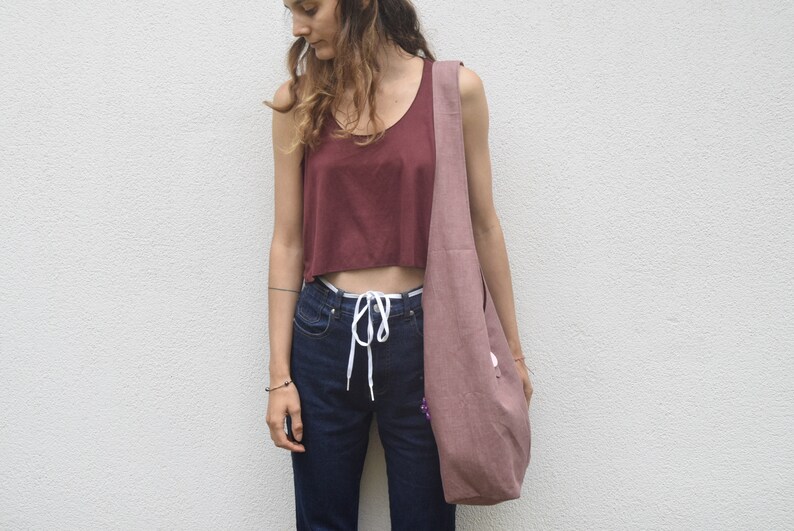 May include: A woman wearing a maroon crop top, blue jeans, and a light pink tote bag with a white drawstring.