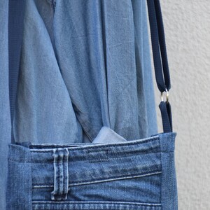 Puede incluir: Un bolso cruzado de mezclilla con una correa azul oscuro y anillos de metal plateado. El bolso presenta un bolsillo frontal hecho de jeans reciclados, incluidos los presillas y costuras originales. El bolso es de mezclilla azul claro.