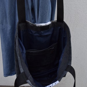 May include: A gray and black tote bag with black straps. The bag is made of denim and has a blue lining. The bag has a small pocket on the inside.