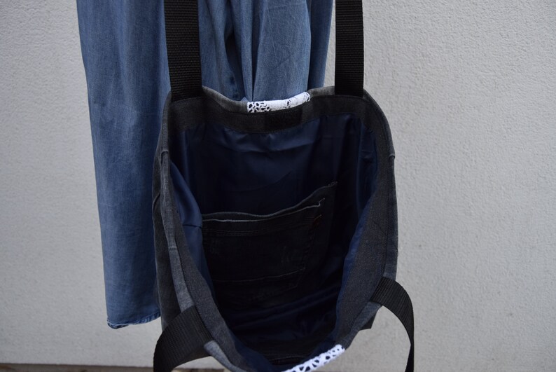 May include: A gray and black tote bag with black straps. The bag is made of denim and has a blue lining. The bag has a small pocket on the inside.