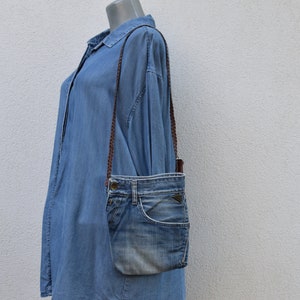 Puede incluir: Un bolso bandolera de mezclilla azul con una correa marr&oacute;n. El bolso est&aacute; hecho de mezclilla reutilizada y tiene un aspecto &uacute;nico y hecho a mano.