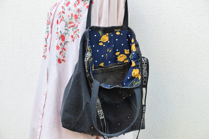 May include: A gray denim tote bag with a floral fabric lining and a black strap with the text "SHINECCI" printed on it. The bag has a pocket on the inside and is decorated with black beads.