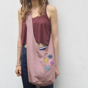 May include: A pink fabric tote bag with a long strap worn over the shoulder. The bag has colorful flower embellishments.