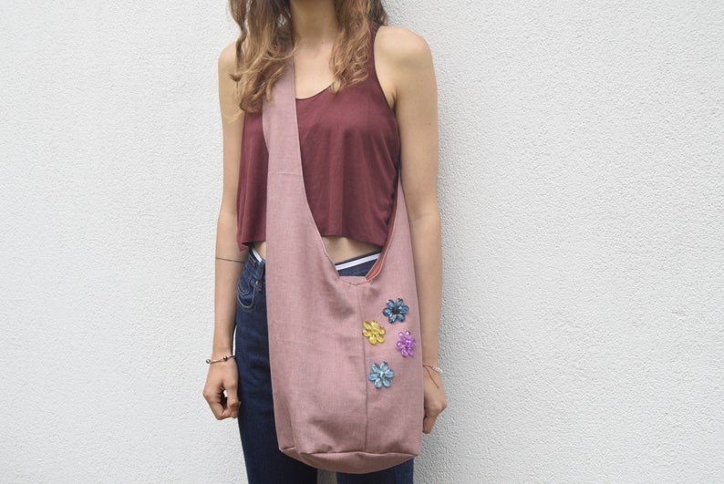 May include: A pink fabric tote bag with a long strap worn over the shoulder. The bag has colorful flower embellishments.