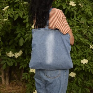 May include: A person wearing a striped shirt and denim overalls is carrying a blue denim tote bag.