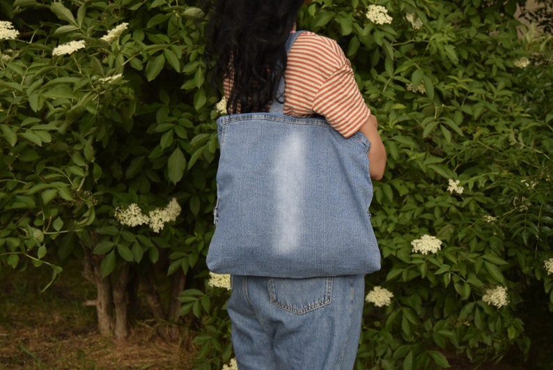 May include: A person wearing a striped shirt and denim overalls is carrying a blue denim tote bag.