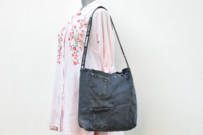 May include: A gray denim tote bag with a long strap featuring the text "SHINECCO" repeated. The bag has multiple pockets and a distressed look.