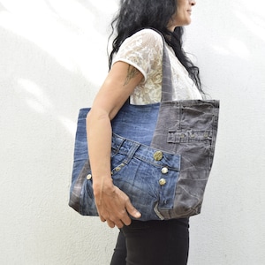 May include: A large tote bag made from recycled denim and fabric. The bag has a blue denim front with a brown fabric back. The bag has a large pocket on the front.