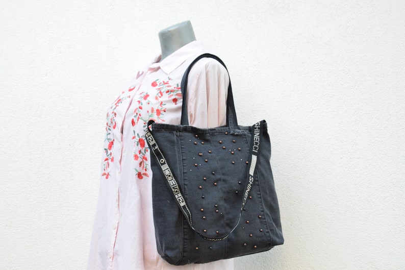 May include: A dark gray denim tote bag with a black strap and silver studs. The strap has the text "Shinecoci" printed on it.