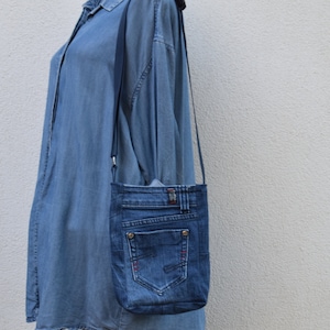 Puede incluir: Un bolso cruzado de mezclilla hecho de jeans reciclados. El bolso presenta un bolsillo trasero, trabillas para el cintur&oacute;n y un cierre de bot&oacute;n. El bolso tiene una correa larga y delgada y es de color azul medio.