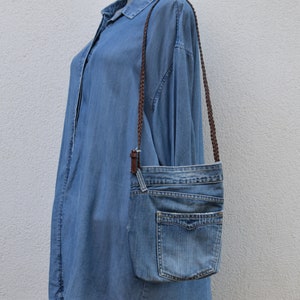 Puede incluir: Un bolso bandolera de mezclilla azul con una correa trenzada marr&oacute;n. El bolso tiene un cierre de solapa y un bolsillo grande en la parte delantera.