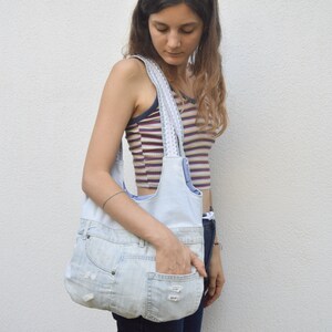 May include: A light blue denim tote bag with white trim and a large pocket on the front. The bag is being held by a person wearing a striped shirt.