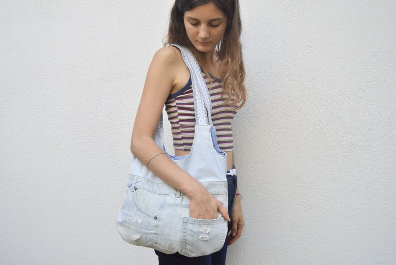 May include: A light blue denim tote bag with white trim and a large pocket on the front. The bag is being held by a person wearing a striped shirt.