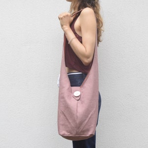 May include: A dusty rose-colored canvas tote bag with a single white button closure. The bag is worn over the shoulder of a person.