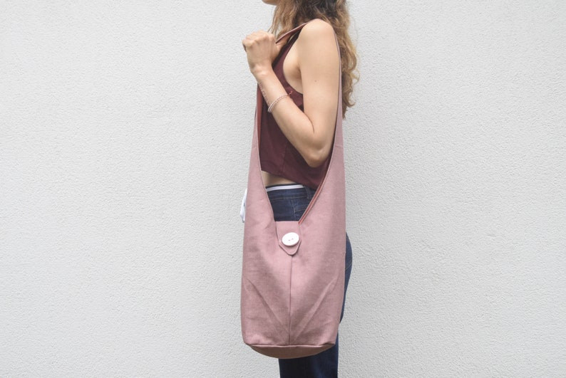 May include: A dusty rose-colored canvas tote bag with a single white button closure. The bag is worn over the shoulder of a person.