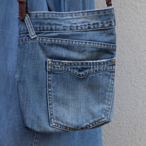 Puede incluir: Un bolso bandolera de mezclilla azul con cierre de solapa y un bolsillo grande en la parte delantera. El bolso tiene una correa de cuero marr&oacute;n.