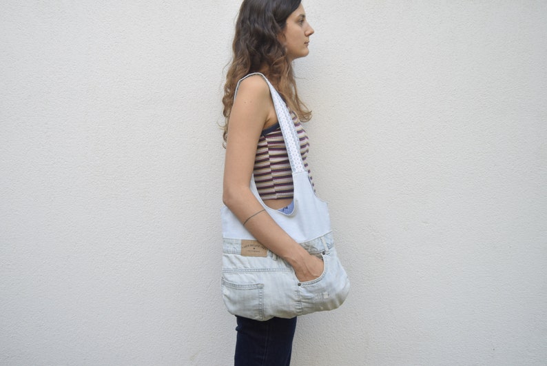 May include: A light blue denim tote bag with a white fabric lining and a white lace trim. The bag is worn over the shoulder of a person wearing a striped shirt.