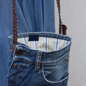 Puede incluir: Un bolso bandolera de mezclilla con una correa trenzada marr&oacute;n y un forro de tela a rayas.