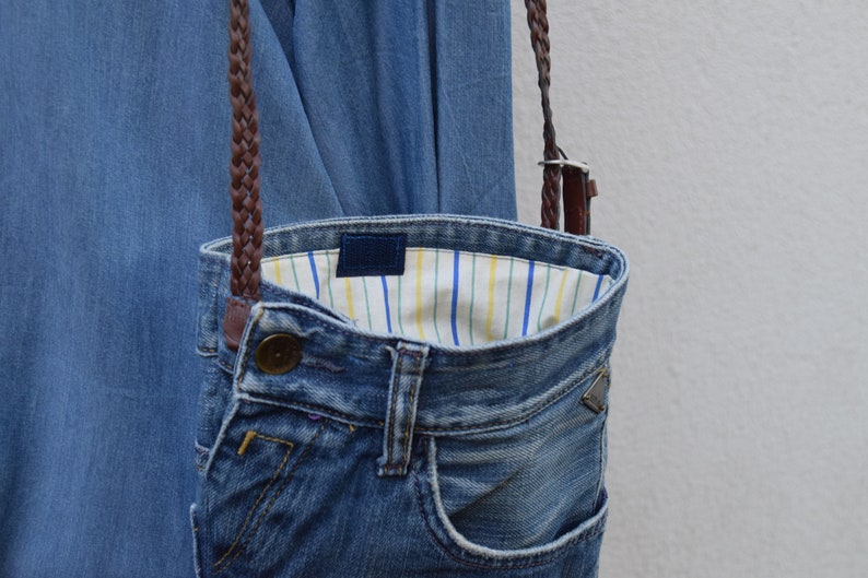 Puede incluir: Un bolso bandolera de mezclilla con una correa trenzada marr&oacute;n y un forro de tela a rayas.