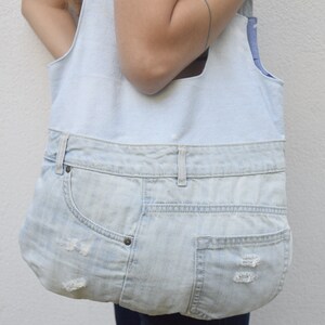 May include: A light blue denim tote bag with a large pocket on the front. The bag is made from recycled denim and has a distressed look.