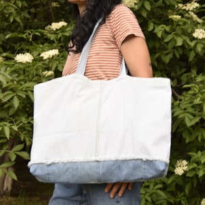 May include: A large white tote bag with a denim bottom. The bag has a frayed edge and is made of a sturdy fabric.