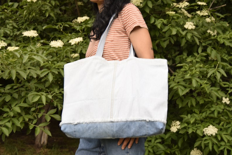May include: A large white tote bag with a denim bottom. The bag has a frayed edge and is made of a sturdy fabric.